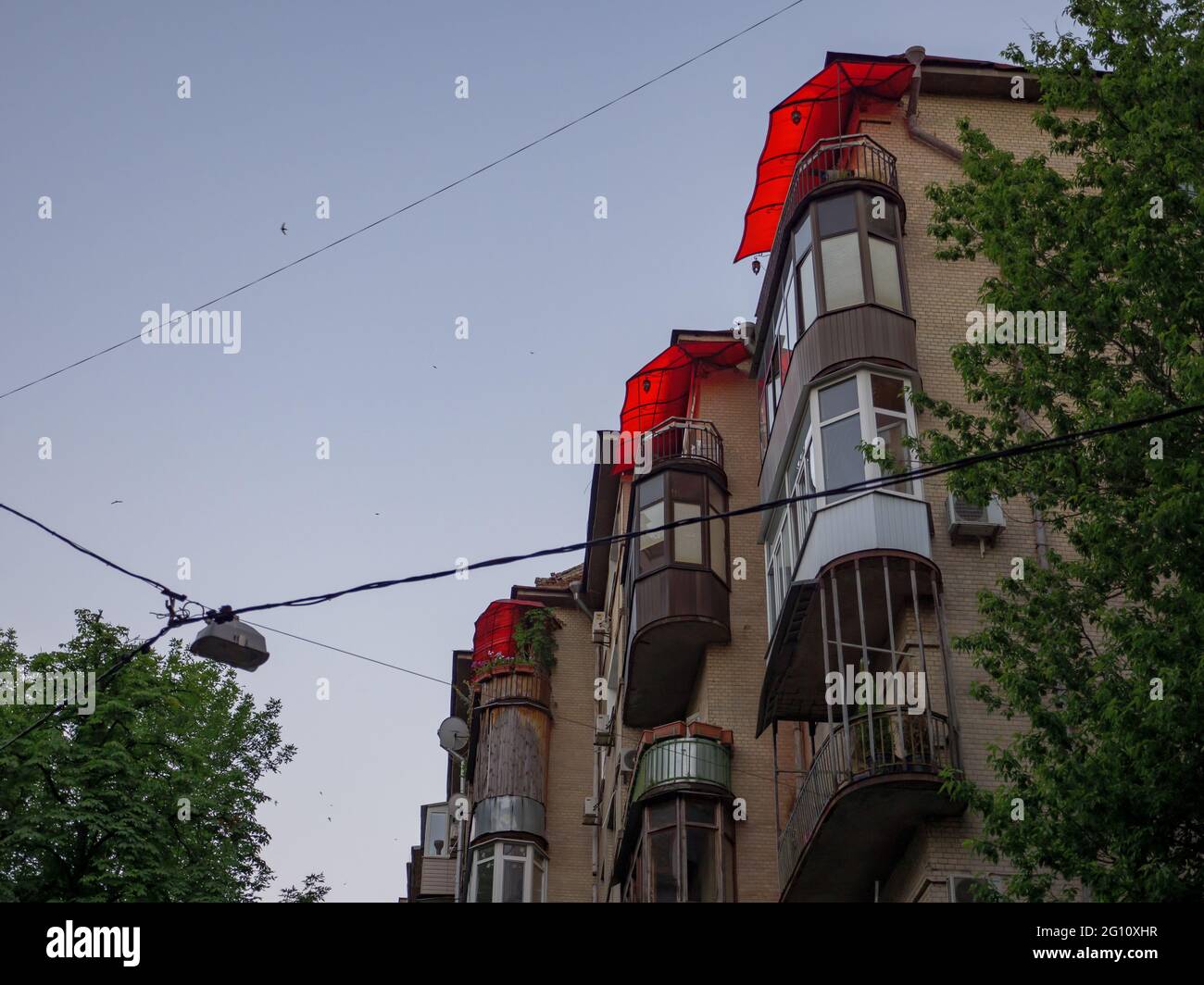 The exterior brick wall of an old soviet period building with beautiful balconies with red open shed sun blinds in the center of Kyiv city. Stock Photo