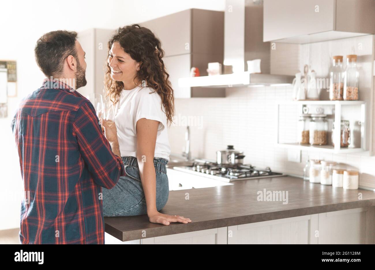 Young couple drinks a glass of white wine in the kitchen - couple in love celebrating their anniversary enjoying their new home Stock Photo