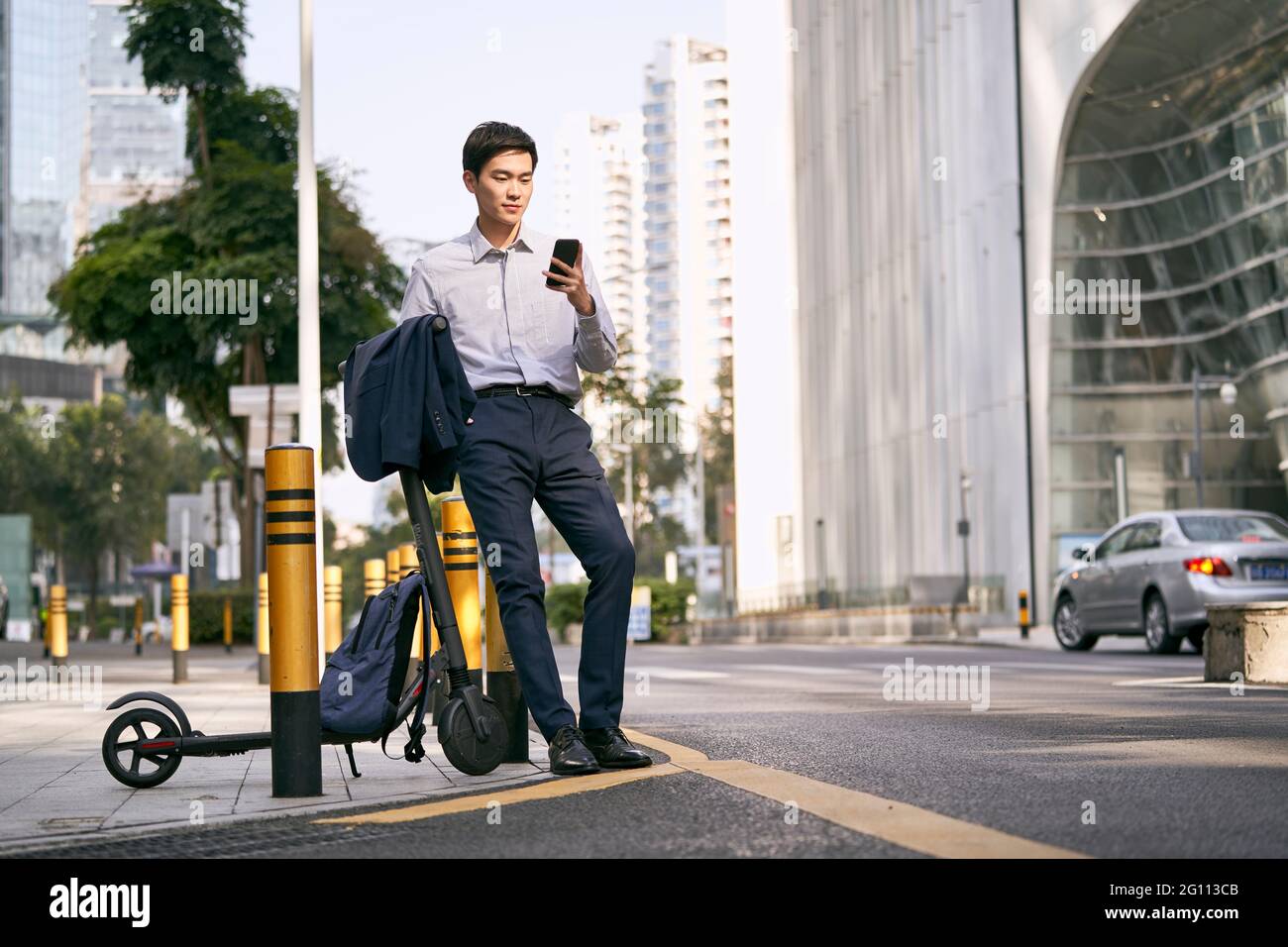 young asian businessman standing next to his electric scooter on street in downtow of modern city Stock Photo