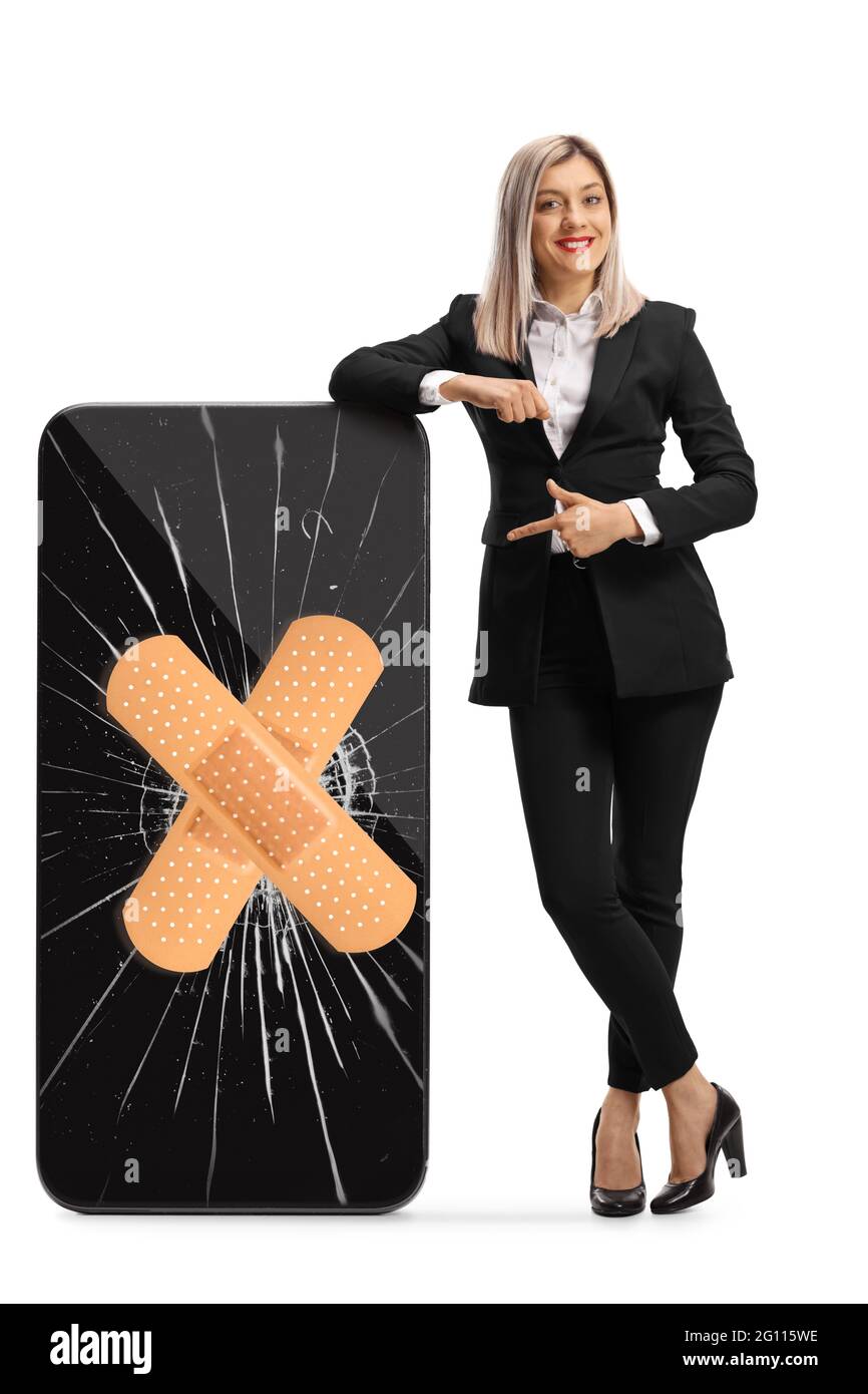 Full length portrait of a businesswoman leaning on a cracked smartphone with bandage and pointing isolated on white background Stock Photo