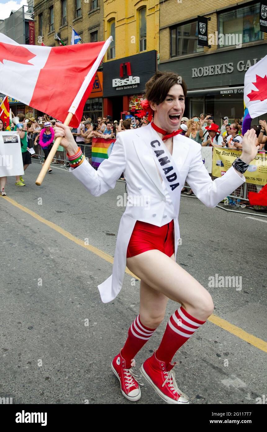 Man holding Canadian National Flag at pride parade Toronto, walking down the street with crowds cheering and celebrating in the background Stock Photo
