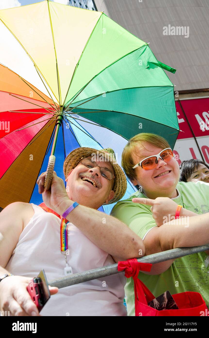 Two men demonstrating at a pride parade.  One is wearing a green shirt and white sunglasses, while the other wears a white shirt and straw hat and hol Stock Photo