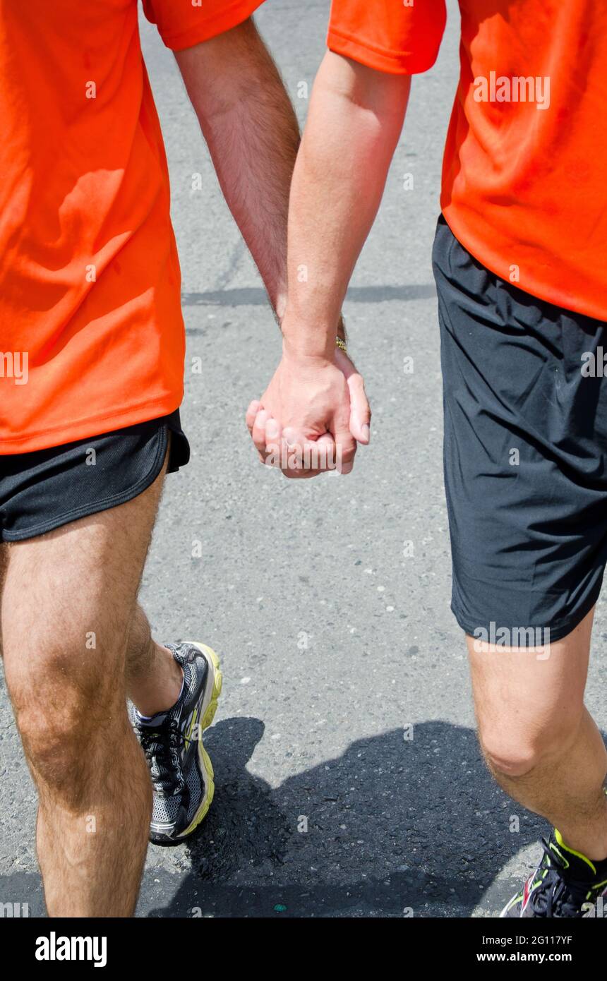 Two men holding hands at pride parade in Toronto, walking down the street dressed in orange and black Stock Photo