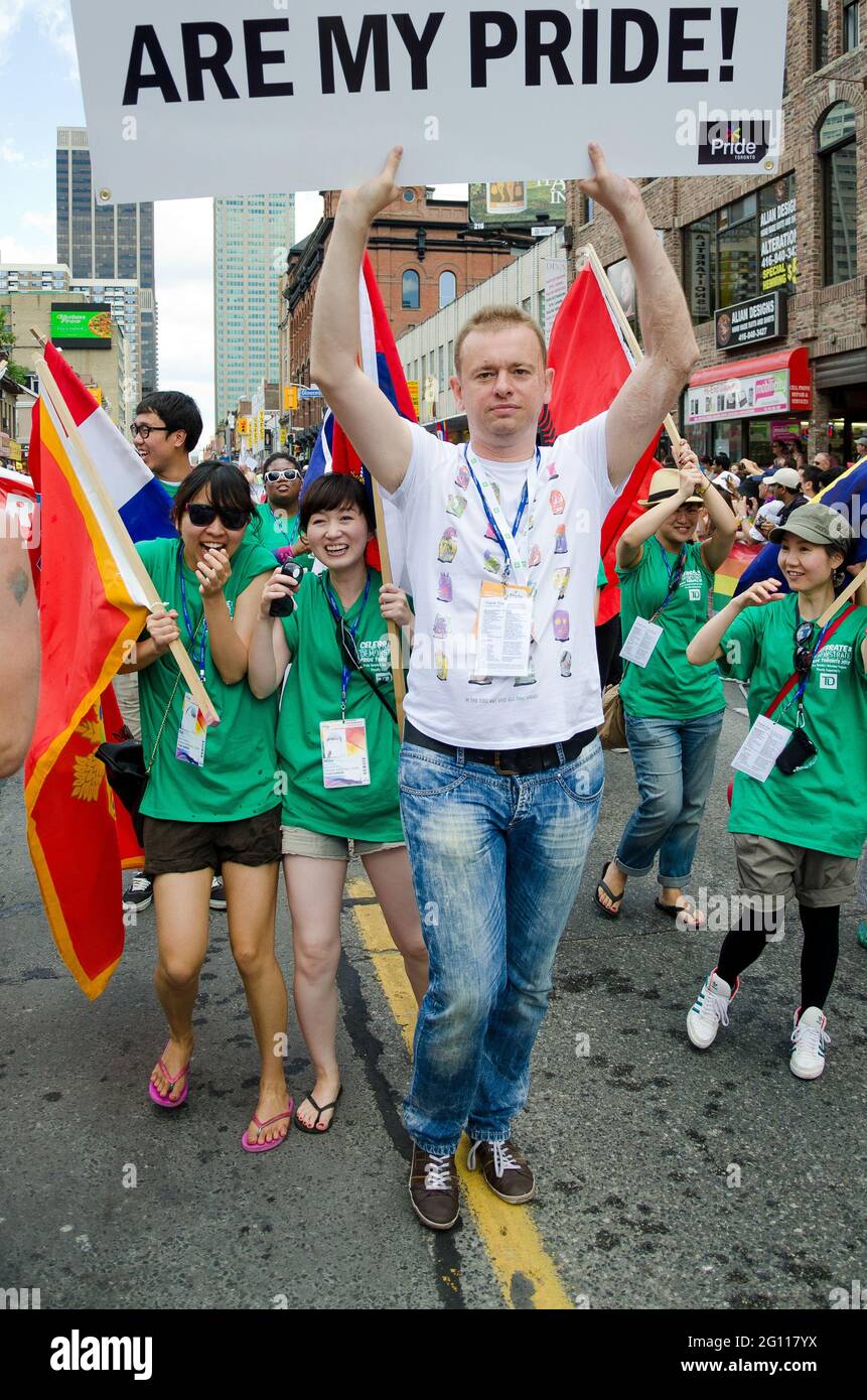Goran Miletic, Grand Marshall leads marchers with banner at pride parade Toronto, brightly dressed men and women walking down the street holding flags Stock Photo
