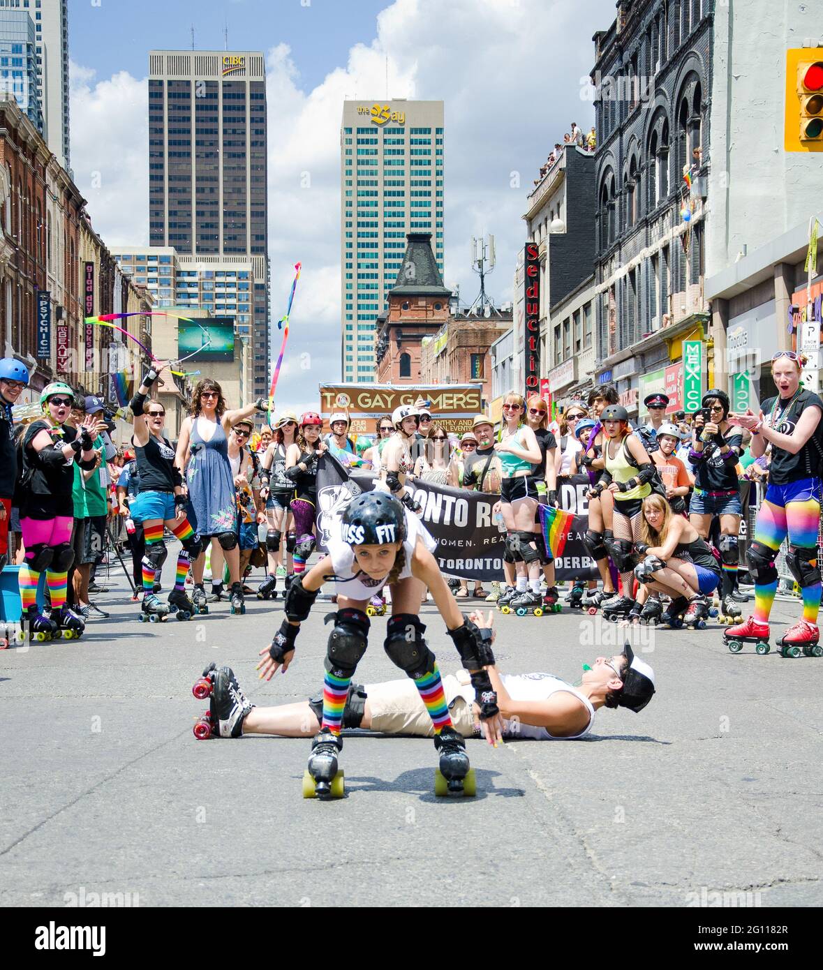 Street performers on skates at pride parade Toronto, with crowds of revelers cheering in the background dressed in rainbow colors and waving flags and Stock Photo