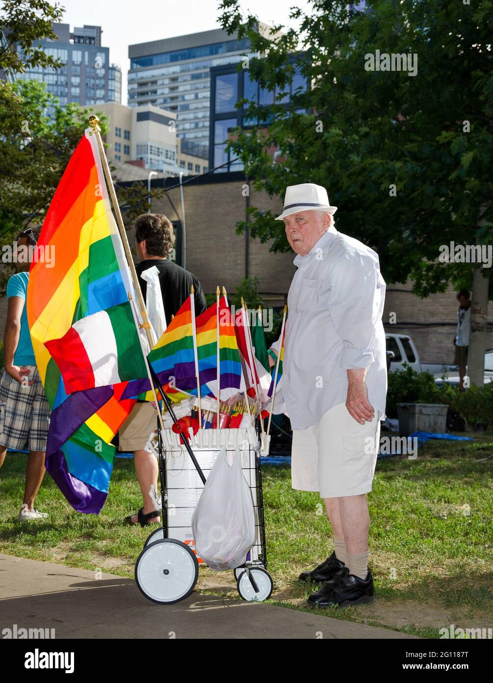 Old man selling rainbow flags at pride parade toronto, standing next to a garden path with a trolley wearing a white hat and dressed in light colors, Stock Photo