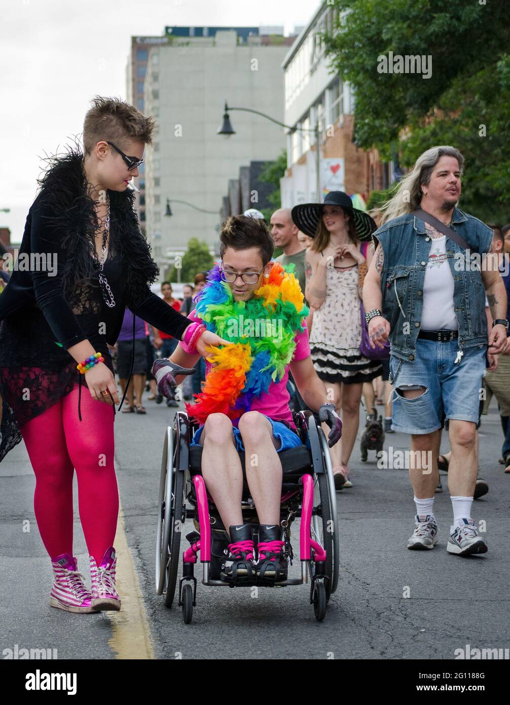 Wheelchair enabled participant in pride parade Toronto, wearing glasses and sporting a rainbow feather scarf going down the street with other marchers Stock Photo