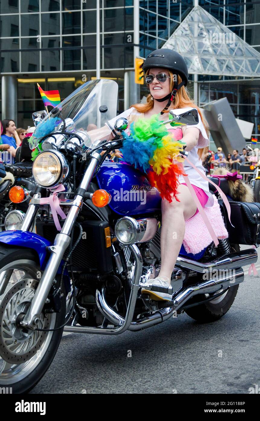Woman biker at pride parade Toronto, riding a blue motorbike in a group, decorated with rainbow colors and sporting helmet and sunglasses Stock Photo