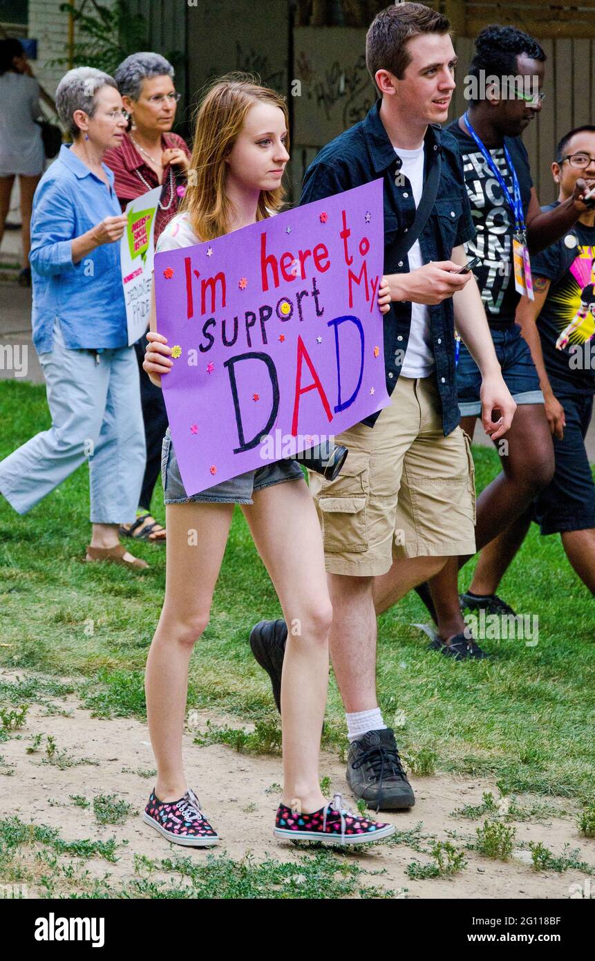 Young girl supporting father at pride parade Toronto,  walking down a garden along with other marchers holding a purple banner Stock Photo