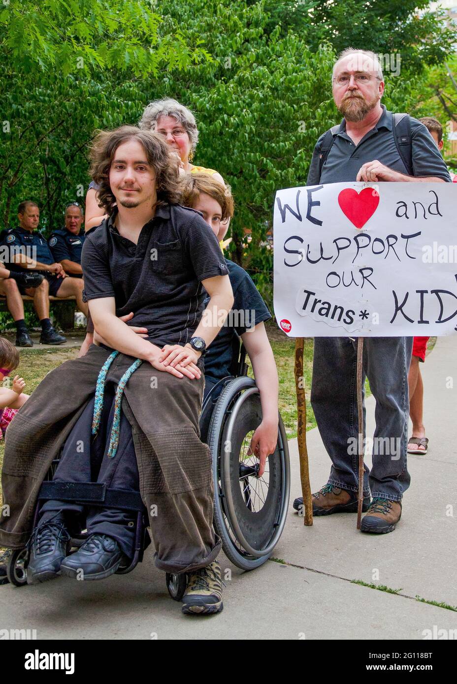 toronto pride parade, transgender kid sitting with wheelchair enabled sibling surrounded by supportive parents holding a banner Stock Photo