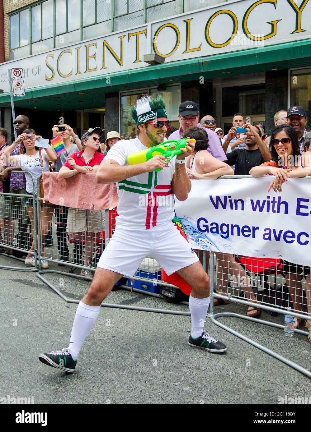 Man with water gun at pride parade in Toronto, laughing as he sprays water onto crowds of cheering and celebrating onlookers Stock Photo