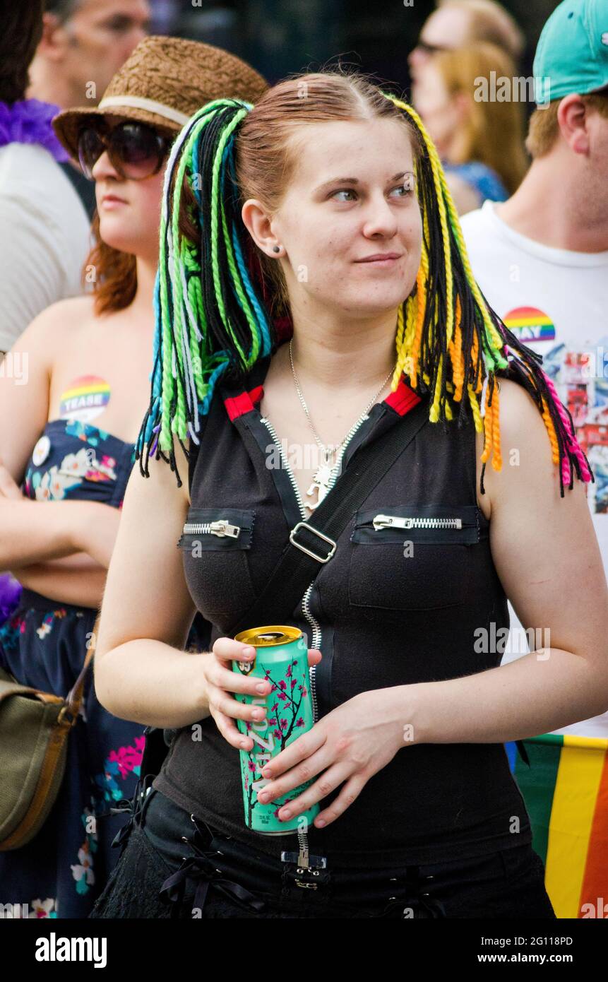Woman at pride parade Toronto, wearing multicolored hair wrap strings with people in the background, medium shot Stock Photo