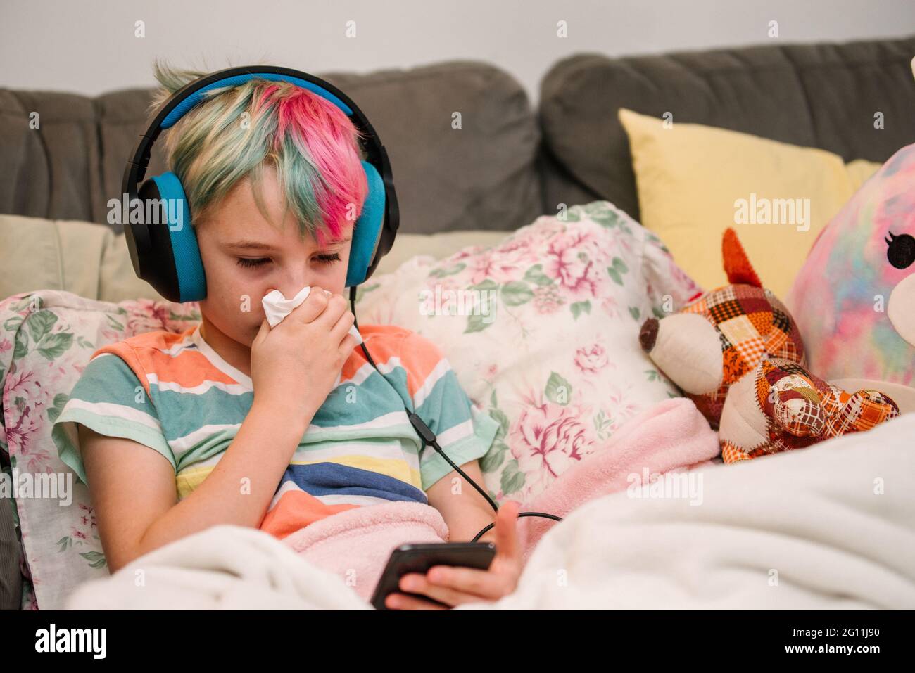 Canada, Ontario, Boy with colorful hair and headphones blowing nose on sofa Stock Photo