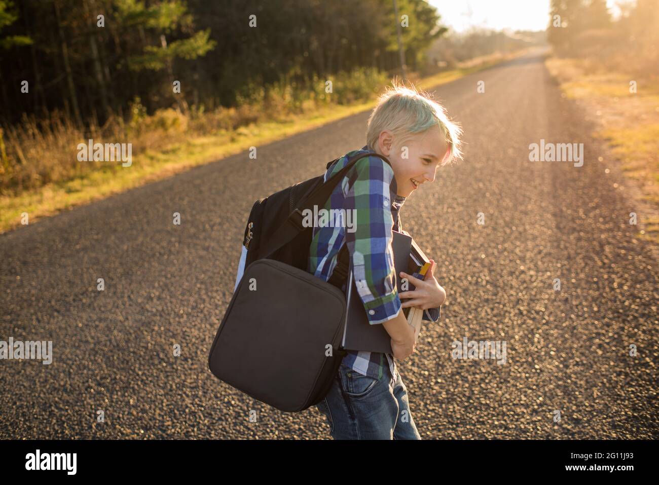 Canada, Ontario, Smiling boy with books on rural road at sunset Stock Photo