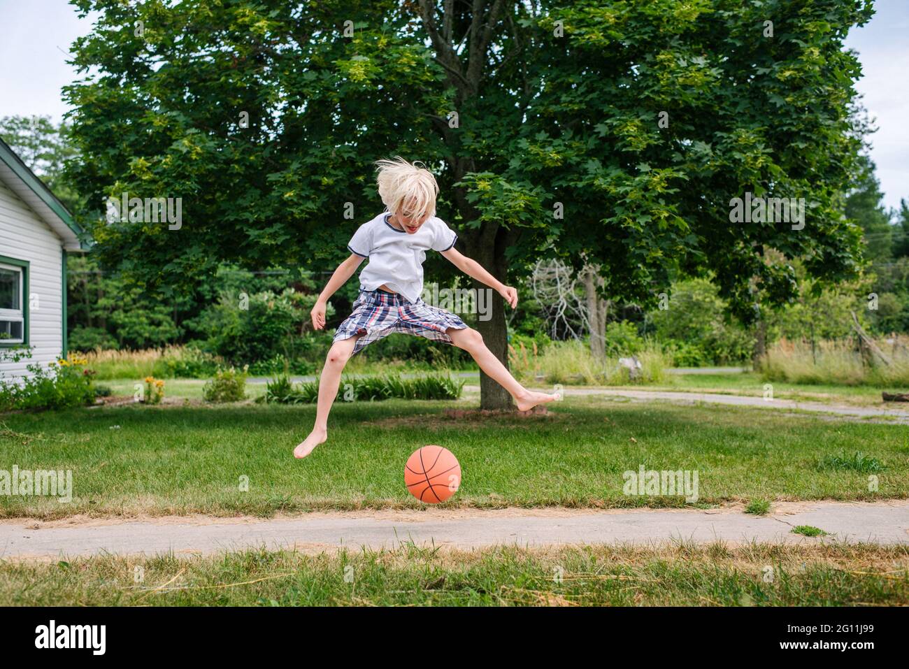Canada, Ontario, Boy jumping over basketball ball outdoors Stock Photo