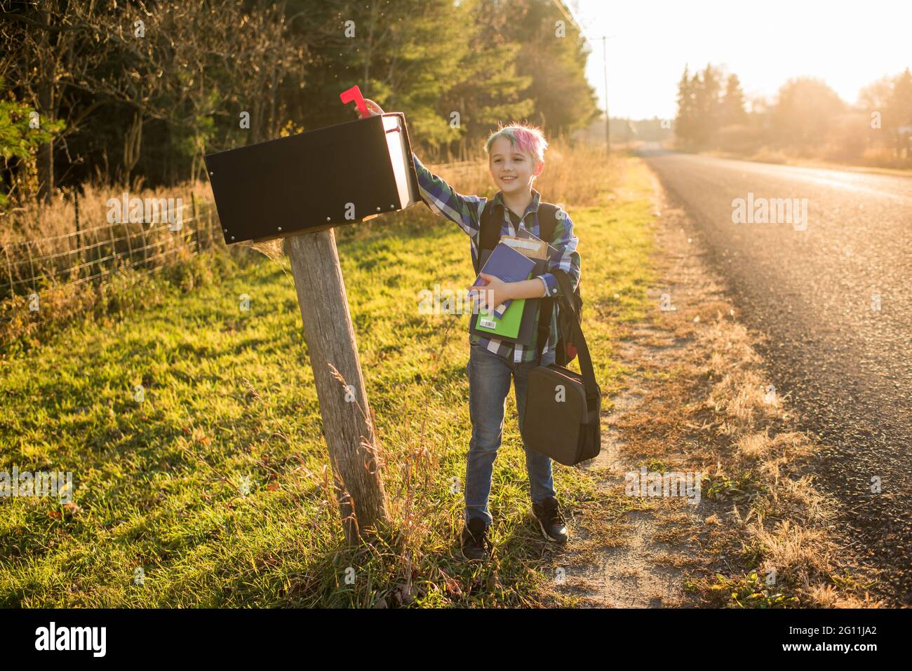 Canada, Ontario, Boy standing at mailbox on roadside at sunset Stock Photo