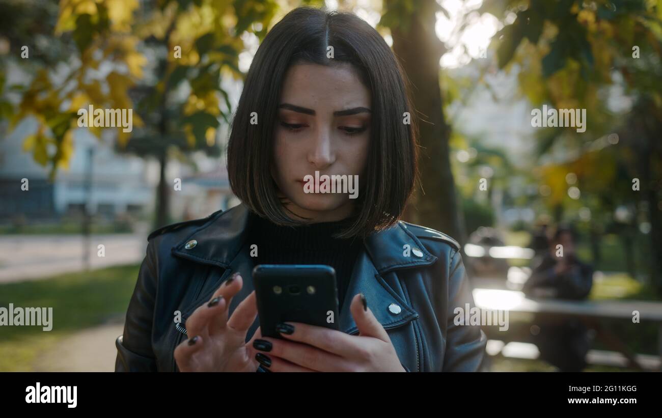 Young unhappy pretty woman wearing a leather jacket is dealing with the phone. Stock Photo
