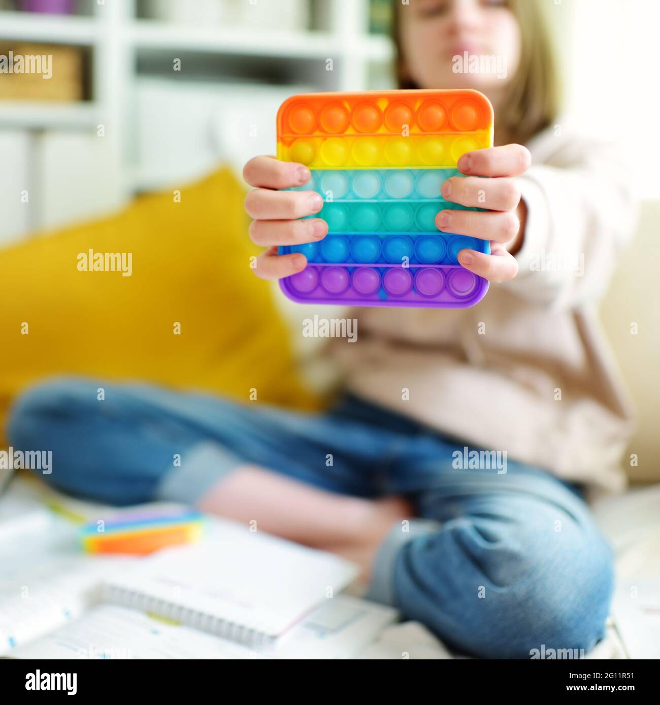 Teenage girl playing with rainbow pop-it fidget toy while studying