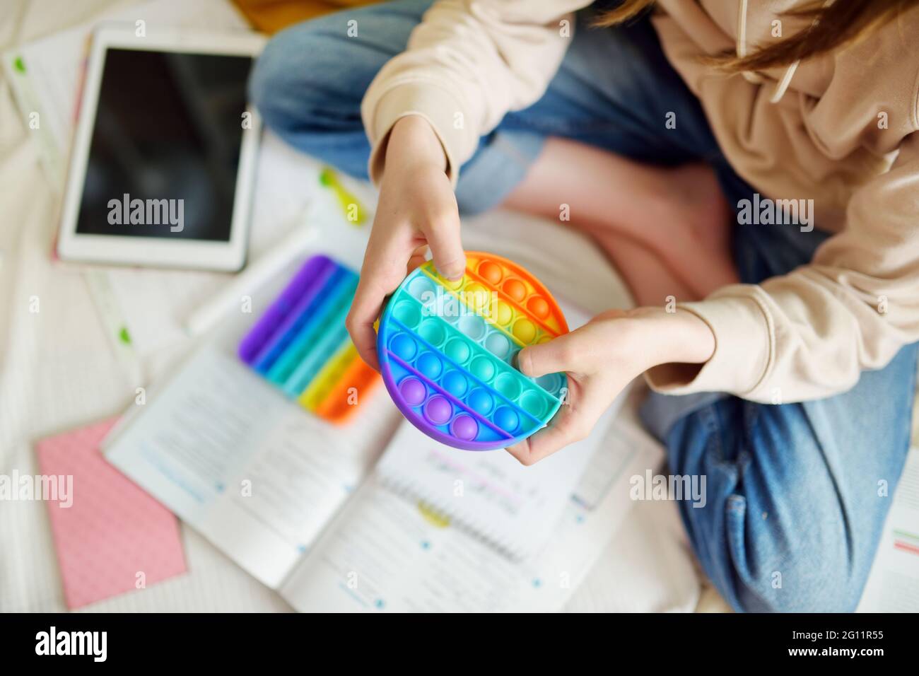 Teenage girl playing with rainbow pop-it fidget toy while studying
