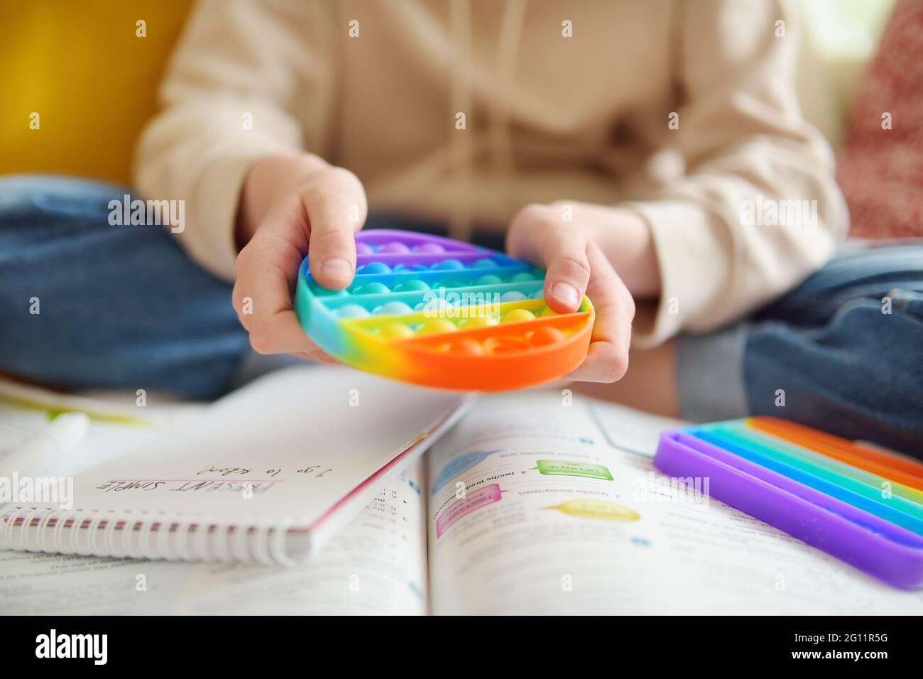 Teenage girl playing with rainbow pop-it fidget toy while studying