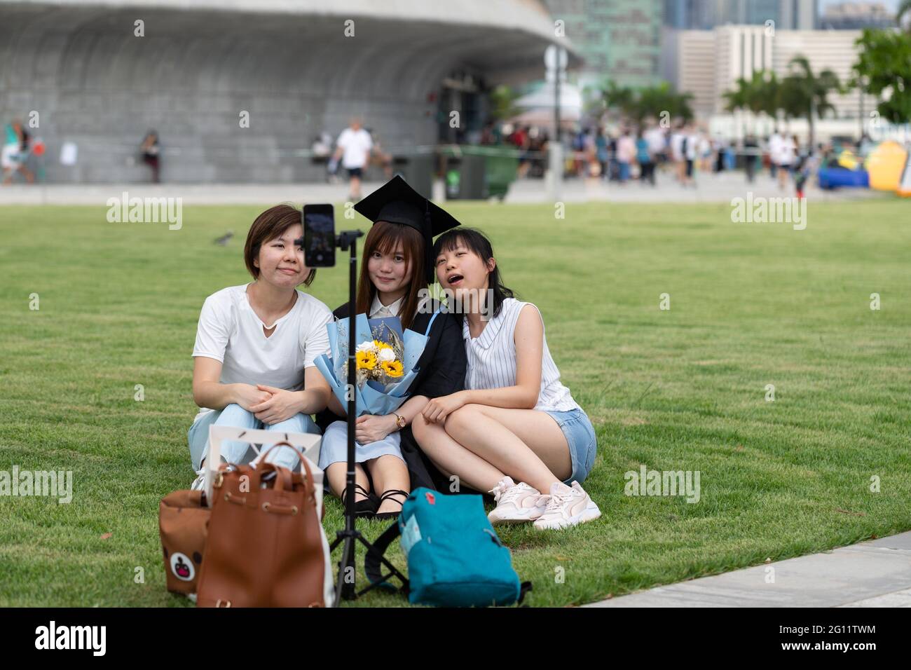 19 5 2021 happy freshly graduated undergraduate and friends in Academic dress gown sit on grass field near West Kowloon Waterfront Promenade, Hong Kon Stock Photo