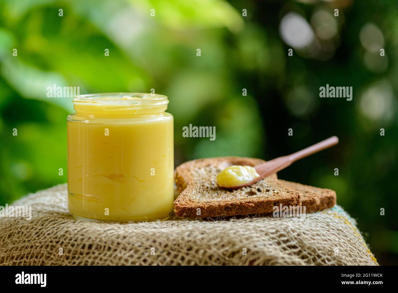 Ghee butter in glass jar with wooden spatula over whole grain bread