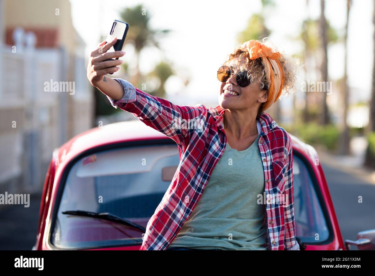 Happy and free adult pretty woman smiling outside her car and taking selfie picture with smartphone - people enjoy life - travel and summer holiday va Stock Photo