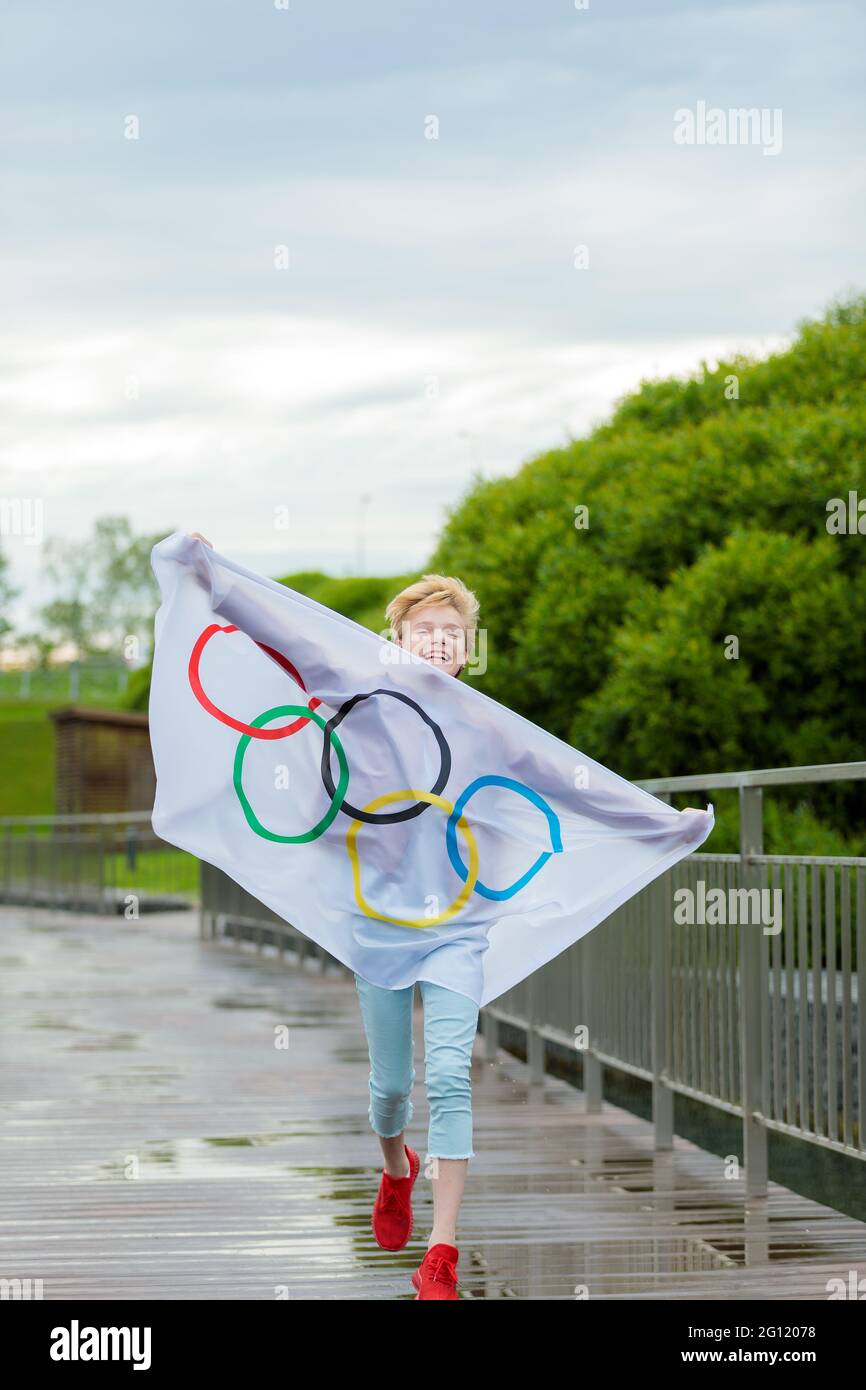 The blonde waving the olympic flag outdoors in the park. Summer Olympic Games. Moscow Russia May 28, 2021 Stock Photo