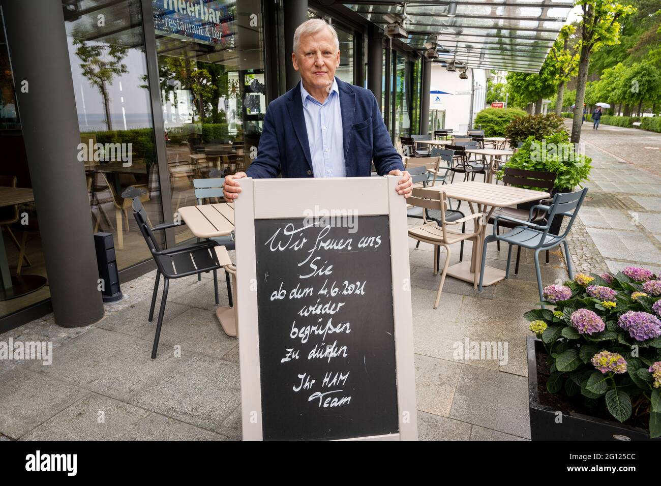 Binz, Germany. 04th June, 2021. Rügen native and hotelier Wolfgang Schewe stands on the terrace of his hotel 'Hotel am Meer & Spa' on the island of Rügen behind a board with the inscription 'We are pleased to welcome you back from 04.06.'. One week after the opening of hotels and other hostels for local holidaymakers, tourists from all over Germany can now come to Mecklenburg-Vorpommern. Credit: Stefan Sauer/dpa/Alamy Live News Stock Photo