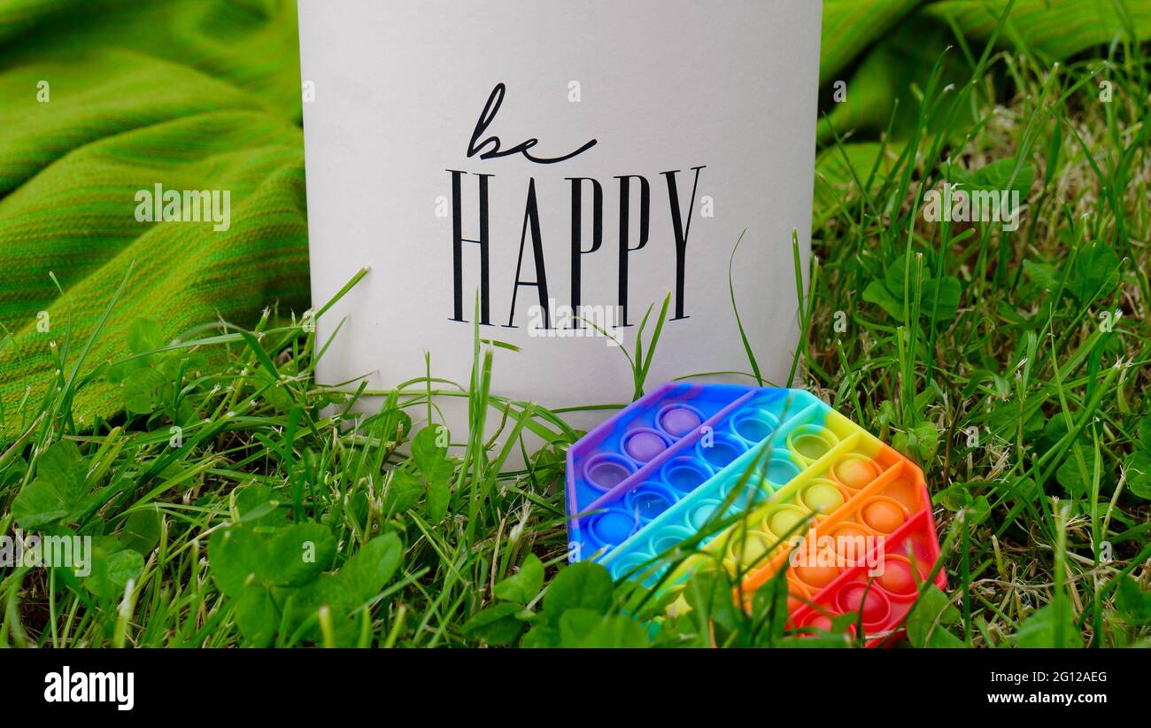 New popular silicone colorful rainbow antistress pop it toy for child on the grass near the gift box with the inscription Be happy. Copy space. Simple dimple Stock Photo