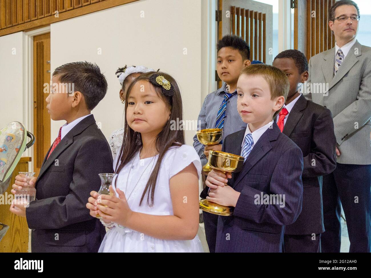 Children in processional at Catholic church.  Four boys and a girl in their Sunday best walk down the aisle to receive communion, while an adult man s Stock Photo