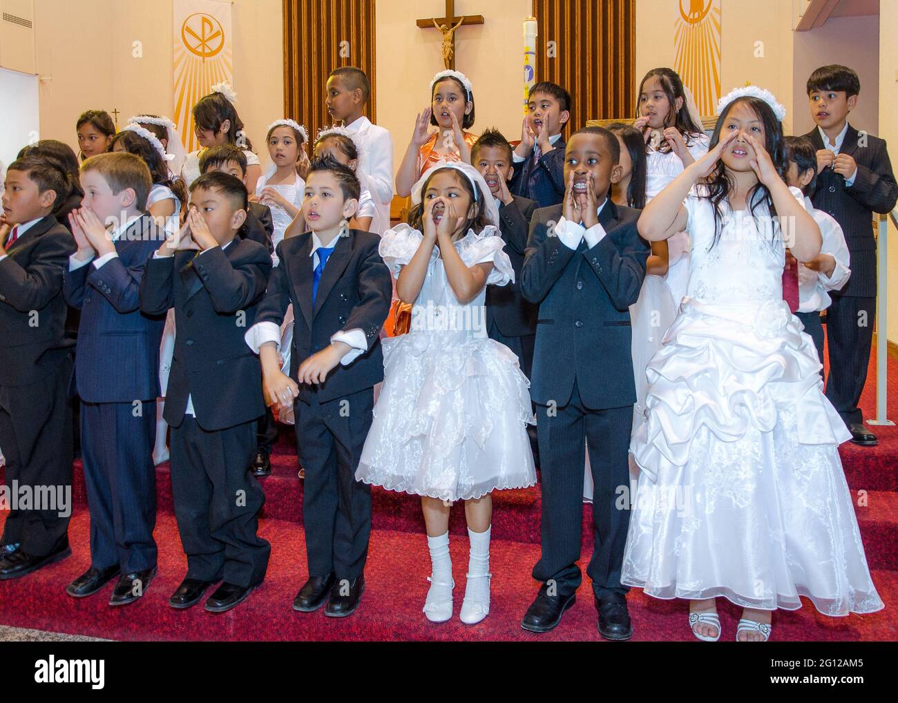 Children in their Sunday best,singing in religious choir at a Catholic church.  Three rows of children stand at the altar of a church in dark suits an Stock Photo