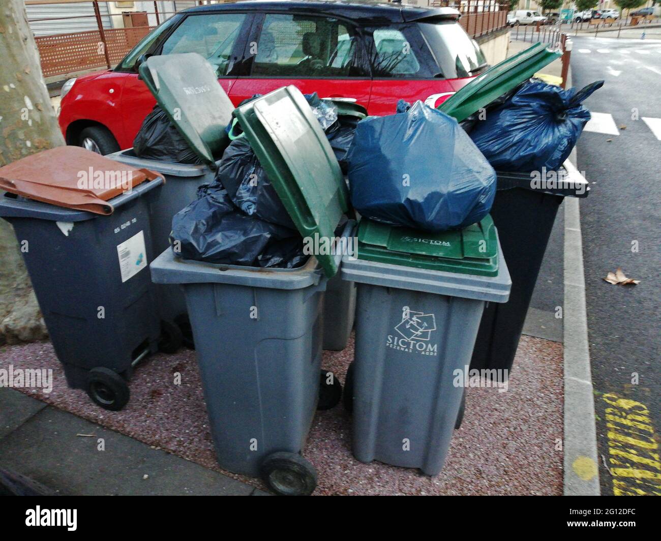 Garbage is piled up around plastic collection bins at a collection point. Stock Photo