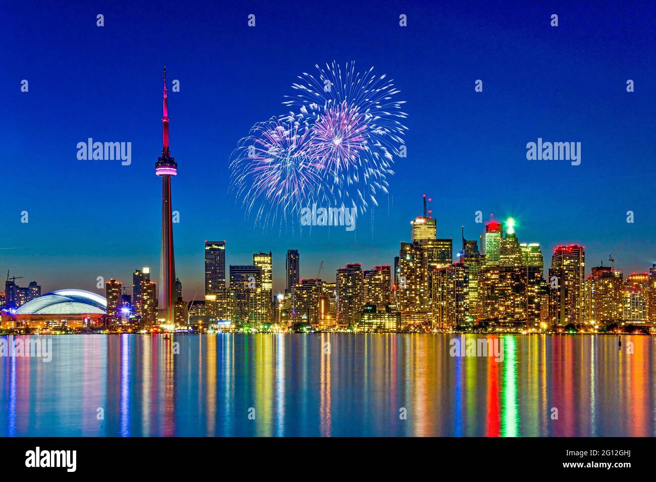 View of Toronto skyline featuring the CN Tower and the Rogers Centre in the dusk hour, beautiful light colors reflected on the lake water Stock Photo