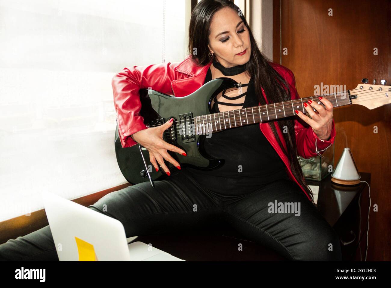 Woman student making virtual presentation by video conference of the progress and learning in the musical performance of the electric guitar industry. Stock Photo