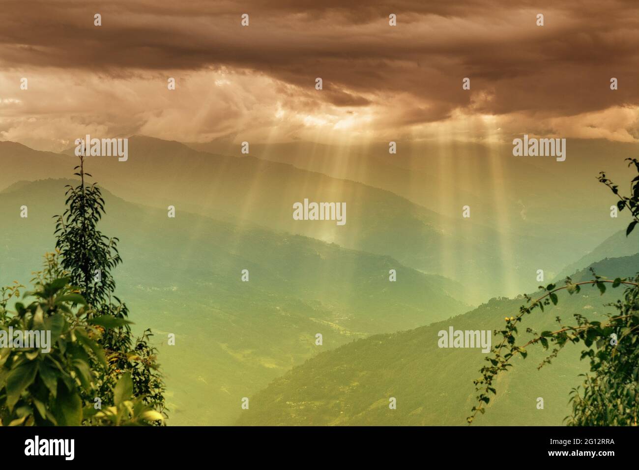 Sun rays coming out of cloud burst - at Rabangla, Sikkim, India. Trees in foreground and Himalayan mountains in background. Stock Photo