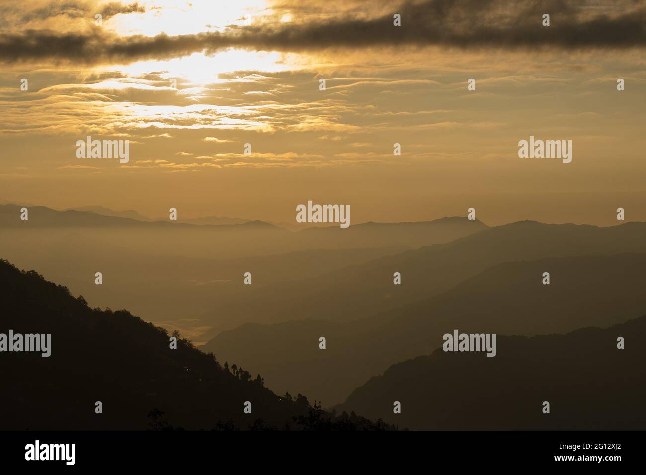 Sunrise scene as seen from Okhrey, Sikkim, India. Sun rising from the back of mountain with orange glow. Fog in the middleground of the picture. Stock Photo