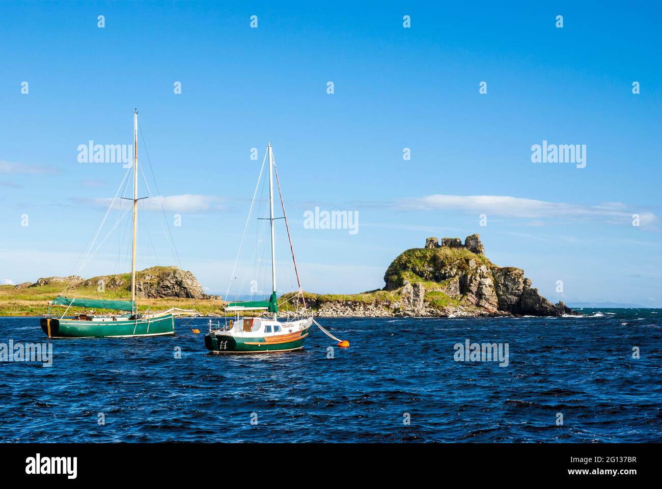 Two boats anchored in Lagavulin Bay on the south coast of the island of Islay, with the ruins of Dunyvaig Castle visible in the background. Stock Photo