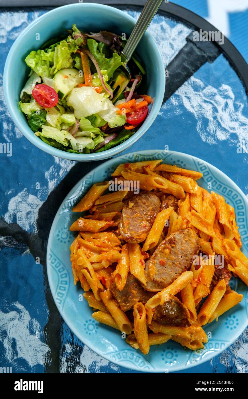 Italian penne alla vodka pink cream sauce with sliced spicy sausage and side salad Stock Photo