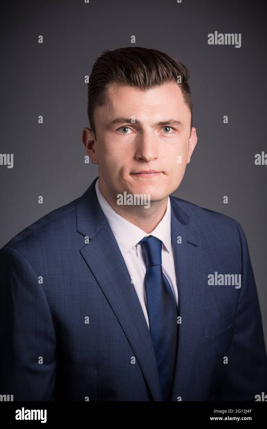 A young man in a corporate portrait. He is unsmiling as he looks at the camera, wearing a suit and tie in his headshot. Stock Photo
