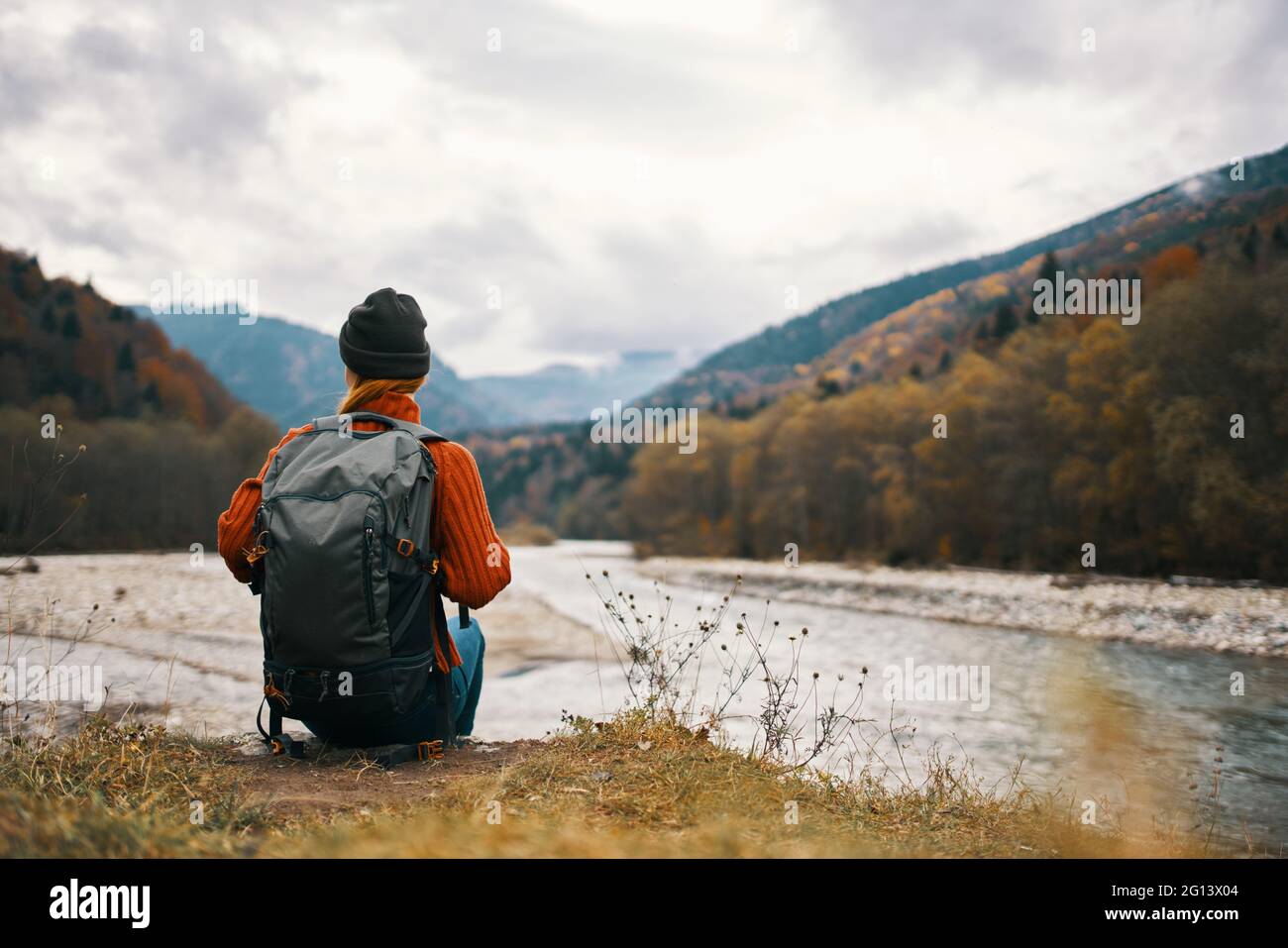 woman with a backpack and in a jacket with a hat on the river bank in ...