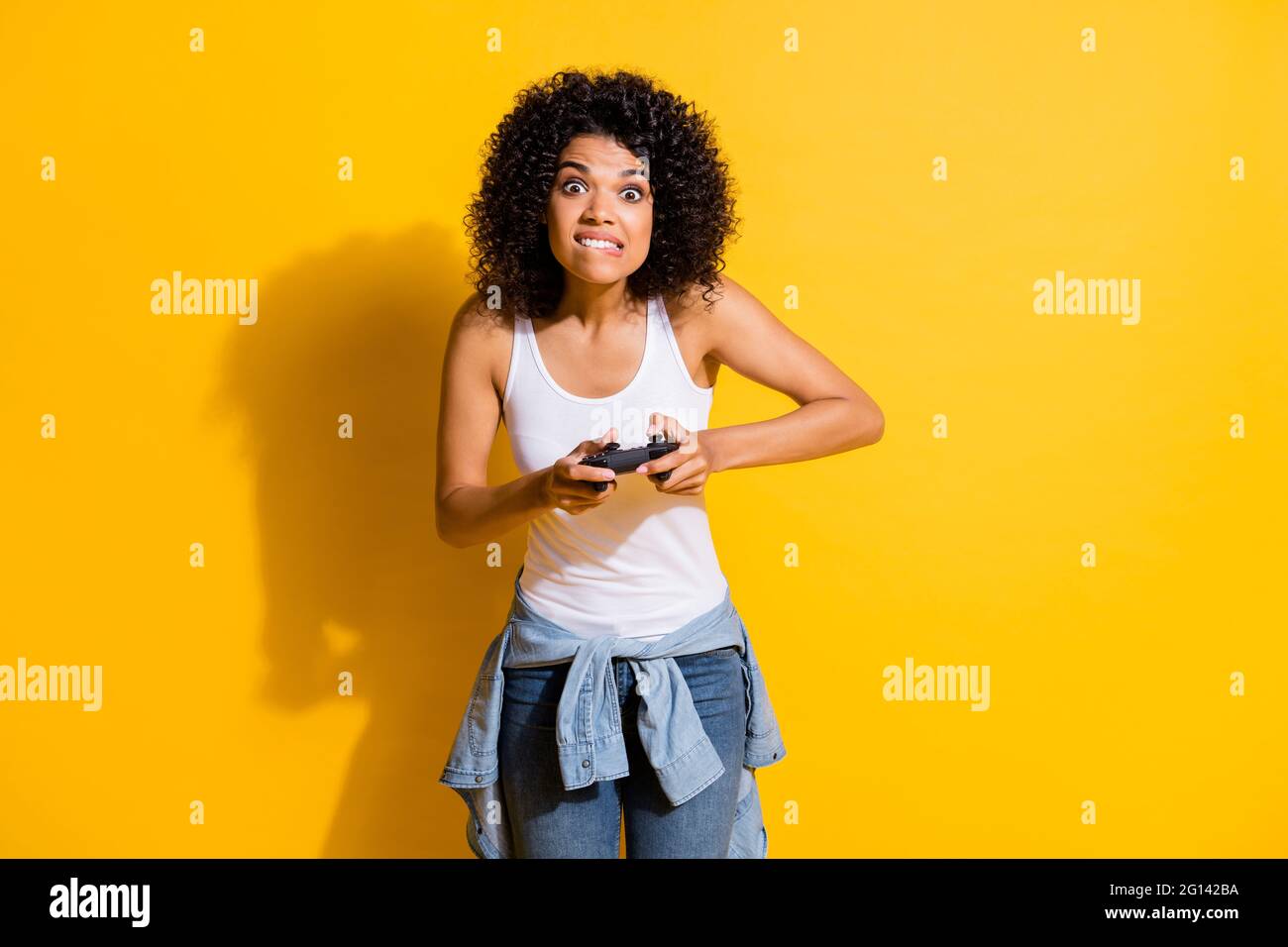Photo of crazy dark skin girl biting lip look interested camera playing games isolated on yellow color background Stock Photo