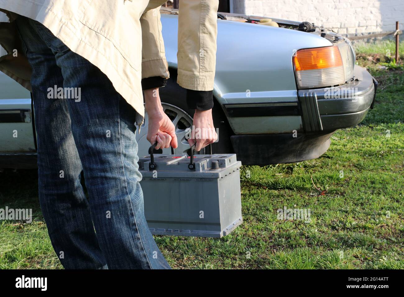 A woman carries a heavy car battery for installation in a car. Stock Photo