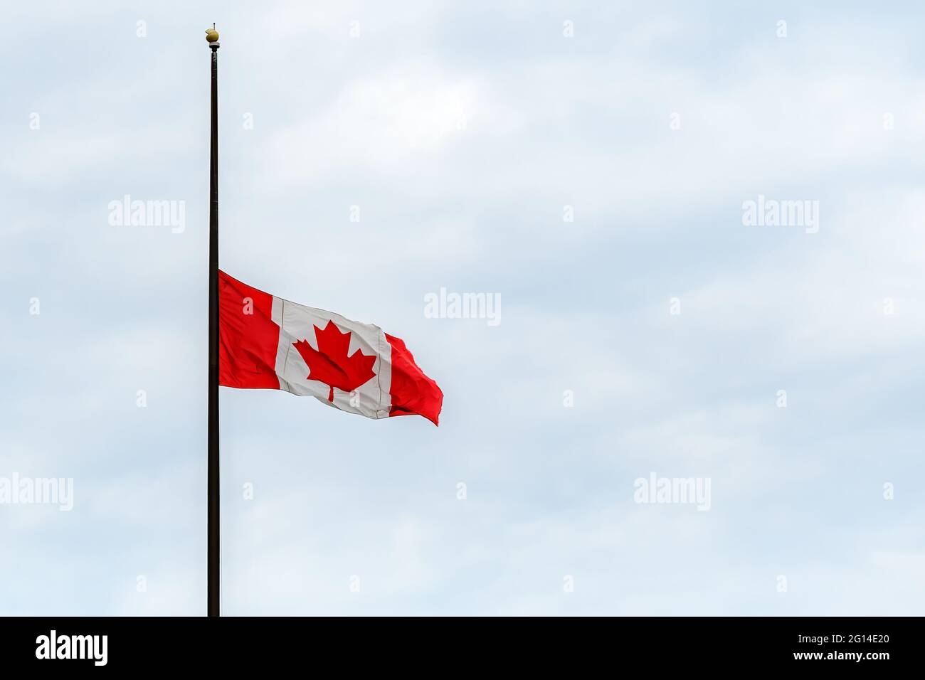 A Canadian flag at half mast, lowered in remembrance of the indigenous children who were abused and dies in residential schools. Overcast, wide view. Stock Photo