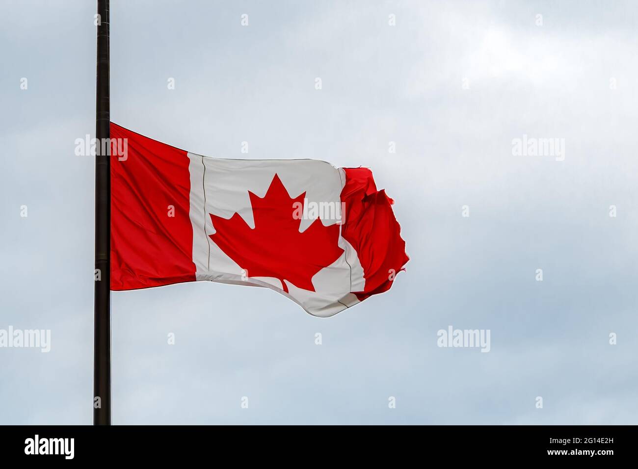 A Canadian flag at half mast, lowered in remembrance of the indigenous children who were abused and dies in residential schools. Overcast, close view. Stock Photo