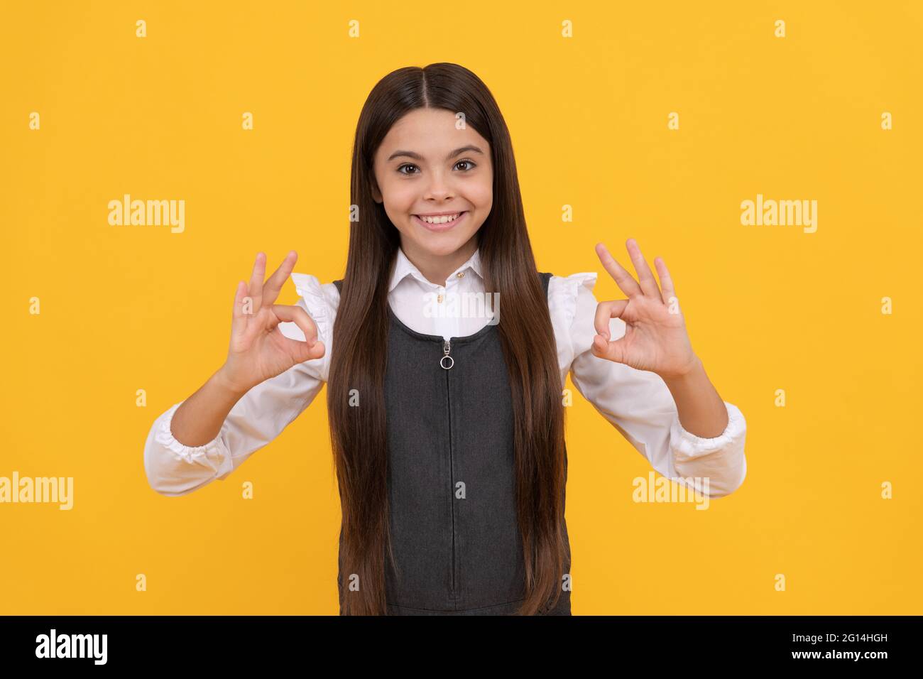 Happy girl child in school uniform smile gesturing double OK sings yellow background, okay Stock Photo