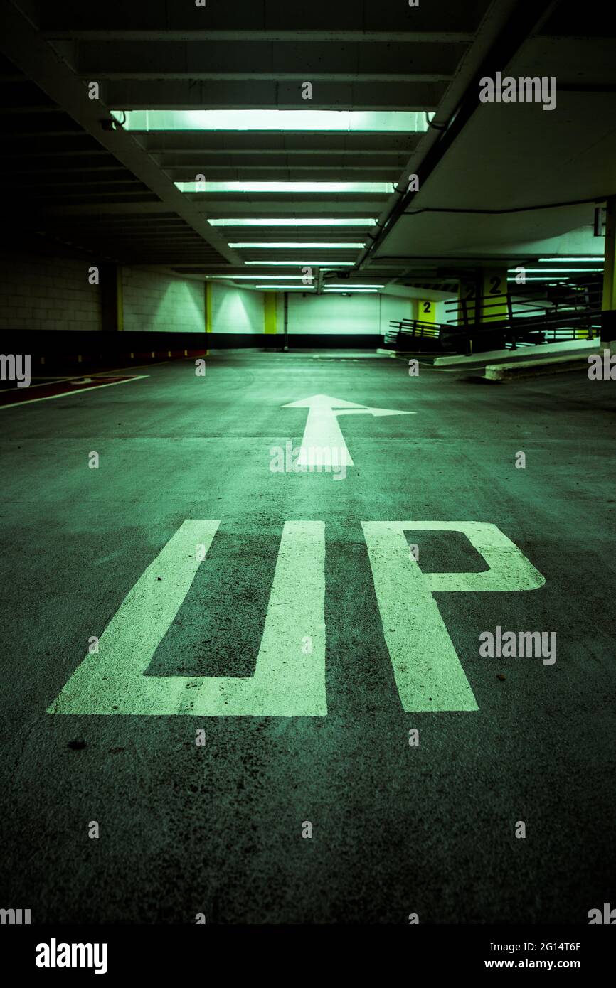 Inside a multi story car park with an up arrow road sign directing traffic upwards to higher levels with green hue lighting Stock Photo