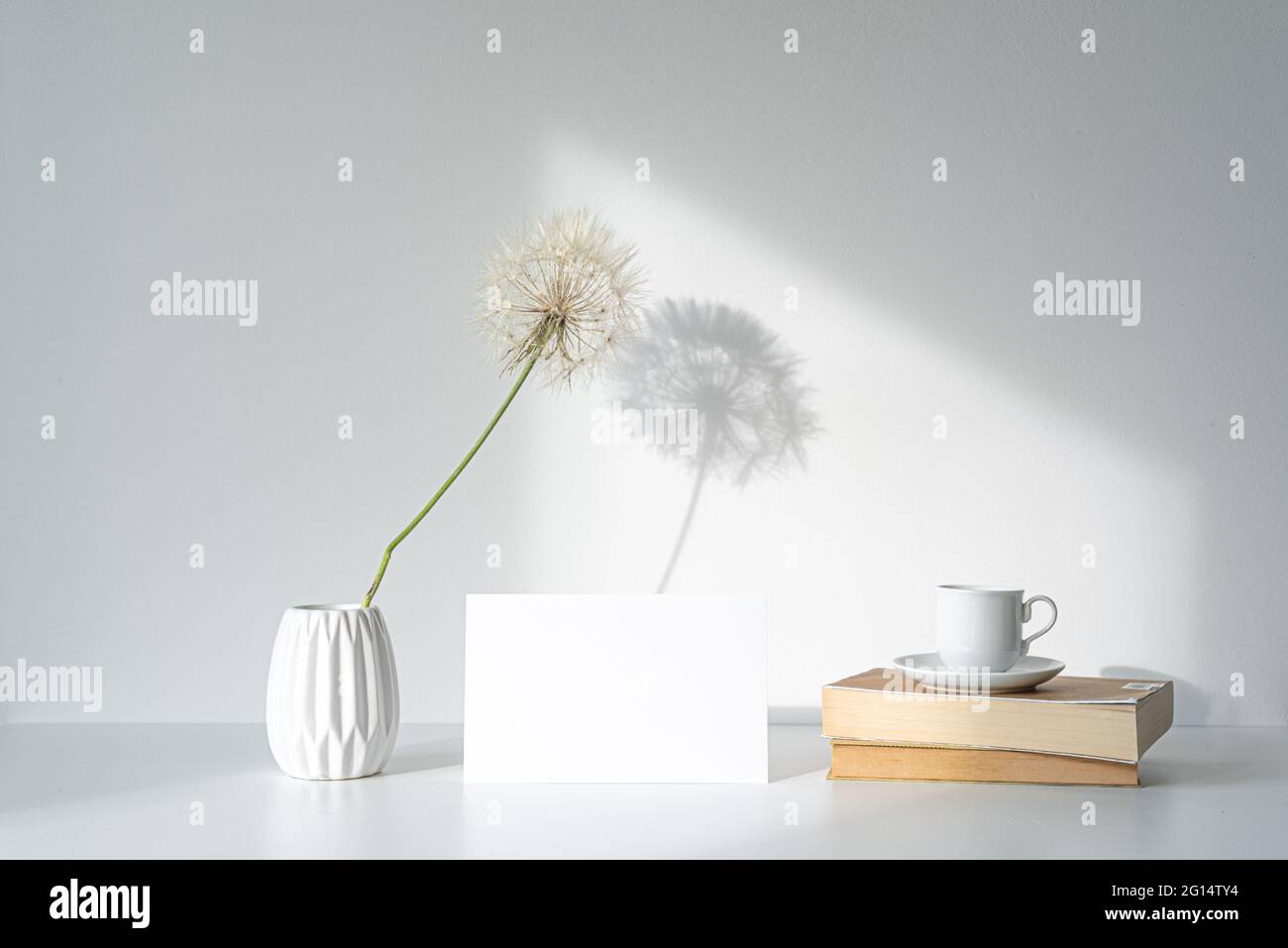 Empty white picture frame mockup in sunlight. Long shadow effect of shower head in the frame. Books and cup of coffee. Elegant lifestyle. White table Stock Photo