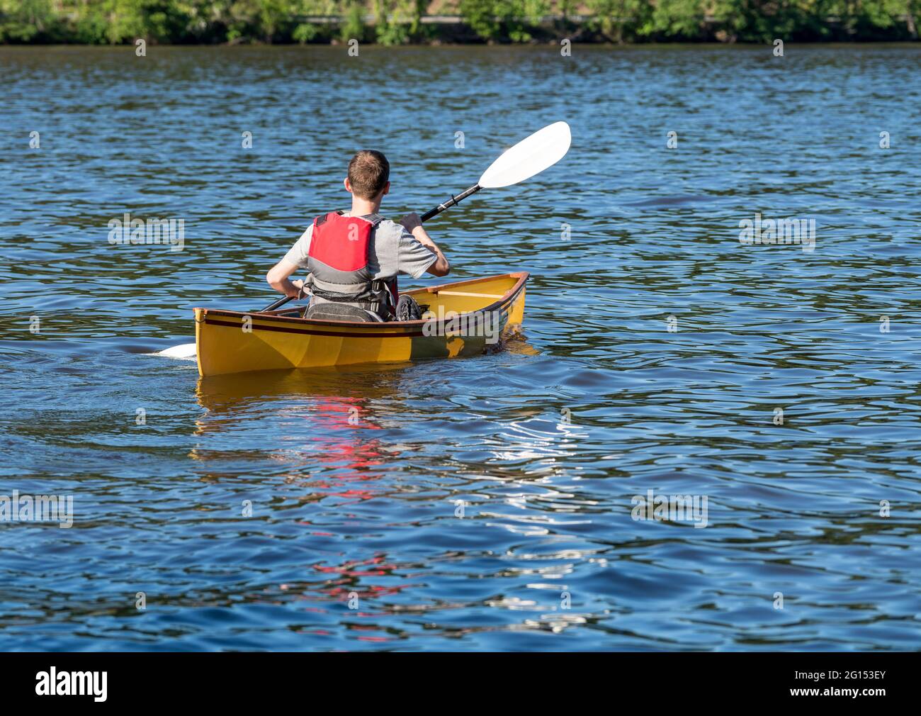 Young man in lifejacket paddling a pack canoe using a kayak paddle on a