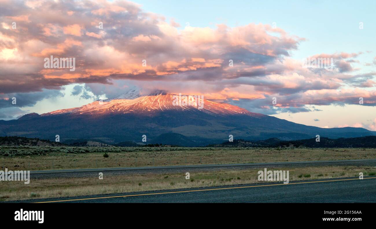 Cumulus clouds capping Mount Shasta & Shastina during sunset, field consisting of natural pasture land. Stock Photo